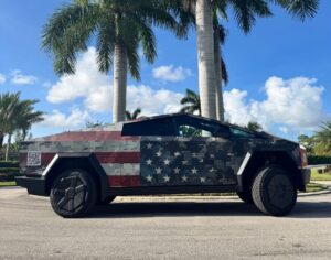 Tesla Cybertruck with American flag digital camouflage wrap parked under palm trees